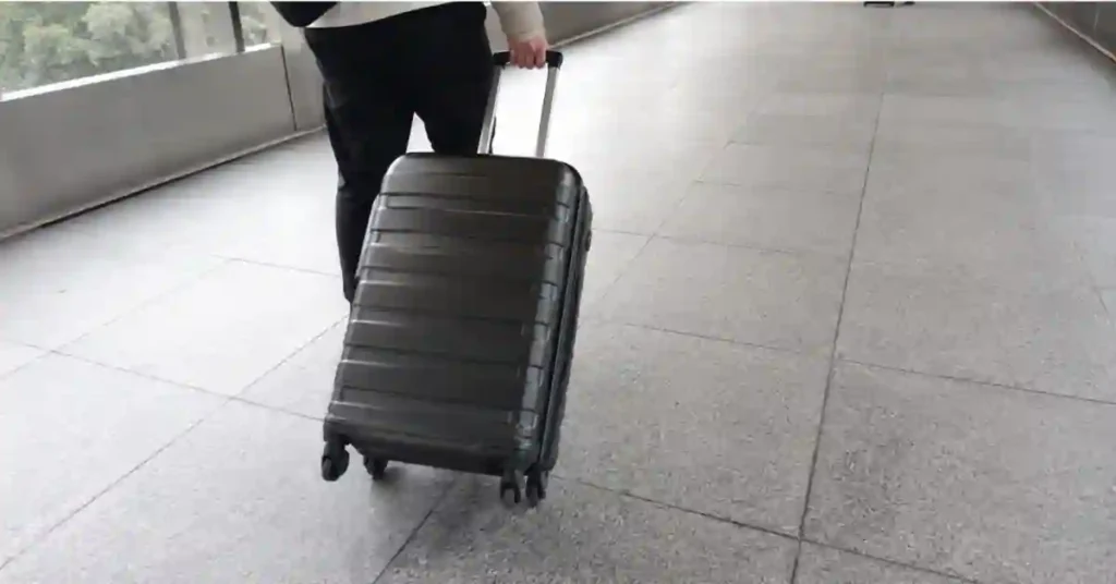 4 Wheel vs 2 Wheel Suitcase: Which One Is Better for Travel in 2026? 7 Traveler tilting a 4-wheel spinner suitcase back onto two wheels