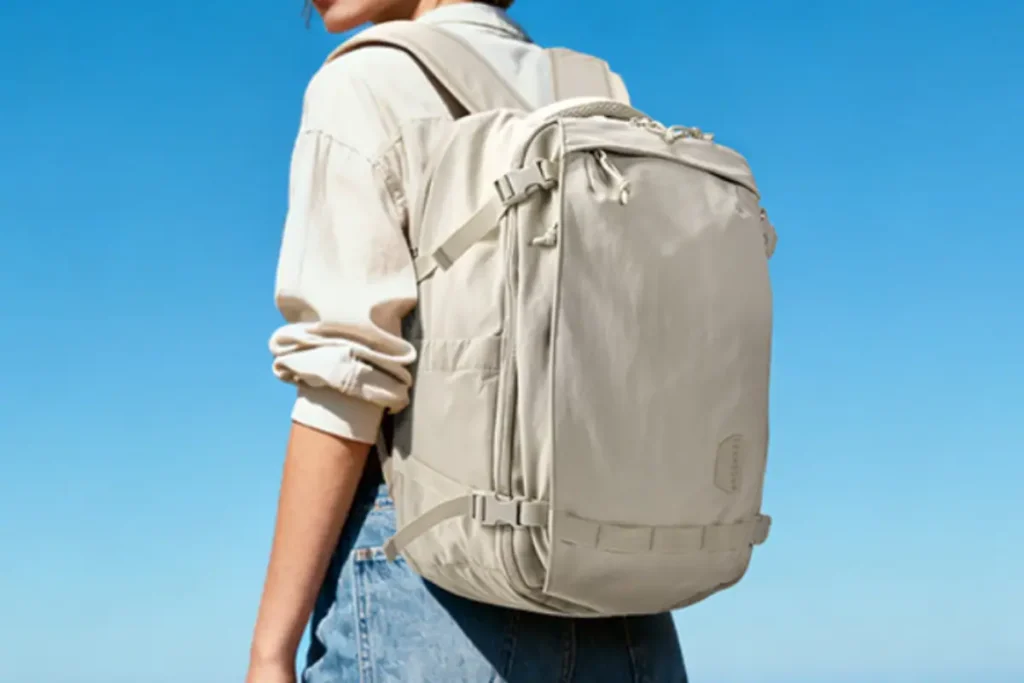 Front view of the BAGSMART Blast 25L travel backpack showing compact airline-friendly design, front quick-access pocket, side water bottle holder, and sleek beige exterior