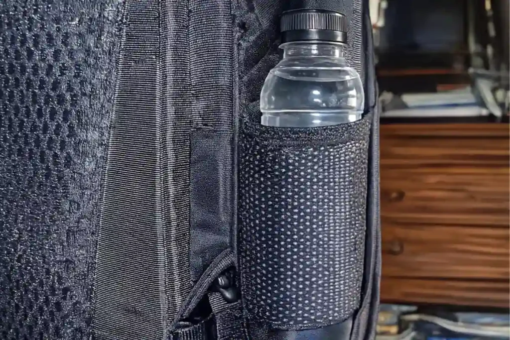 Close-up of a black travel backpack showing a mesh side pocket holding a water bottle, highlighting easy-access hydration storage.